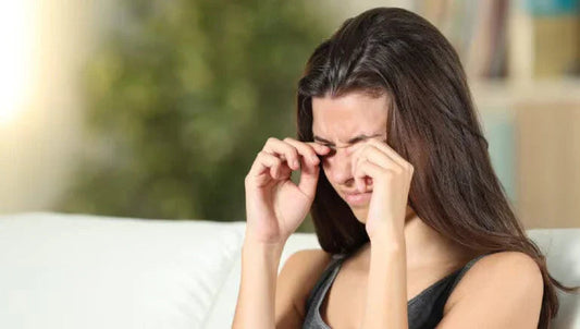 Vrouw wrijft in jeukende ogen op bank, allergie of oogirritatie symptoom.