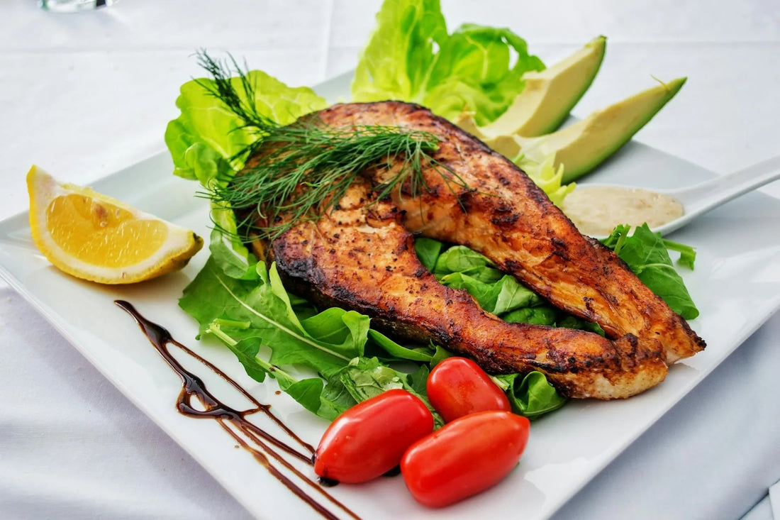 Gegrilde zalmfilet met citroen, avocado, salade en cherrytomaten op een wit bord