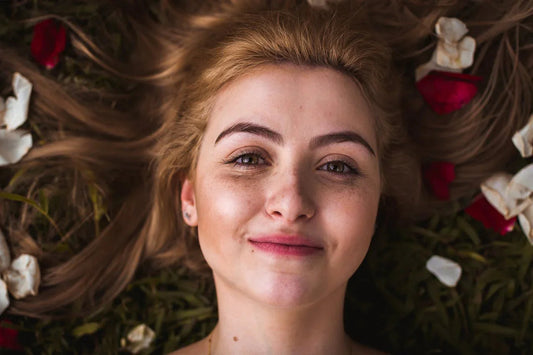 Vrouw met blond haar ligt in het gras tussen witte en rode rozenblaadjes, close-up portret.