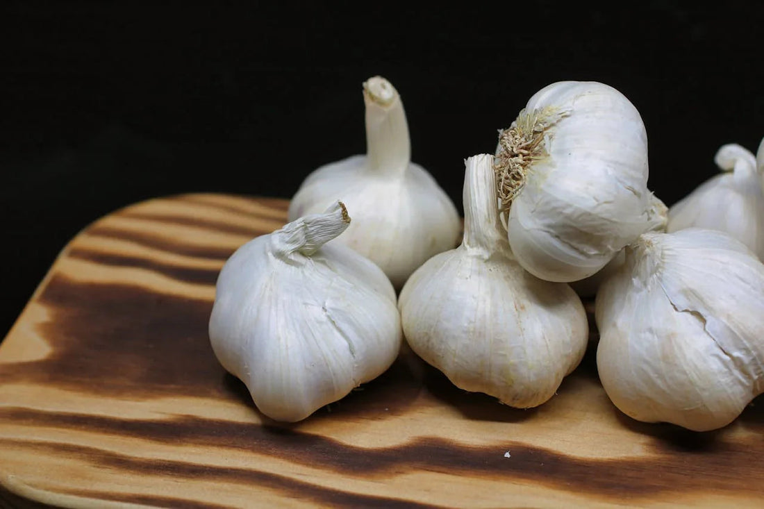 Knoflookbollen op houten snijplank, vers knoflook tegen zwarte achtergrond