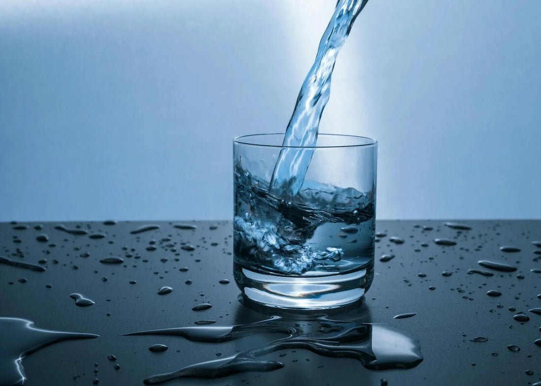 Glas water wordt ingeschonken op zwarte tafel met gemorste druppels, close-up