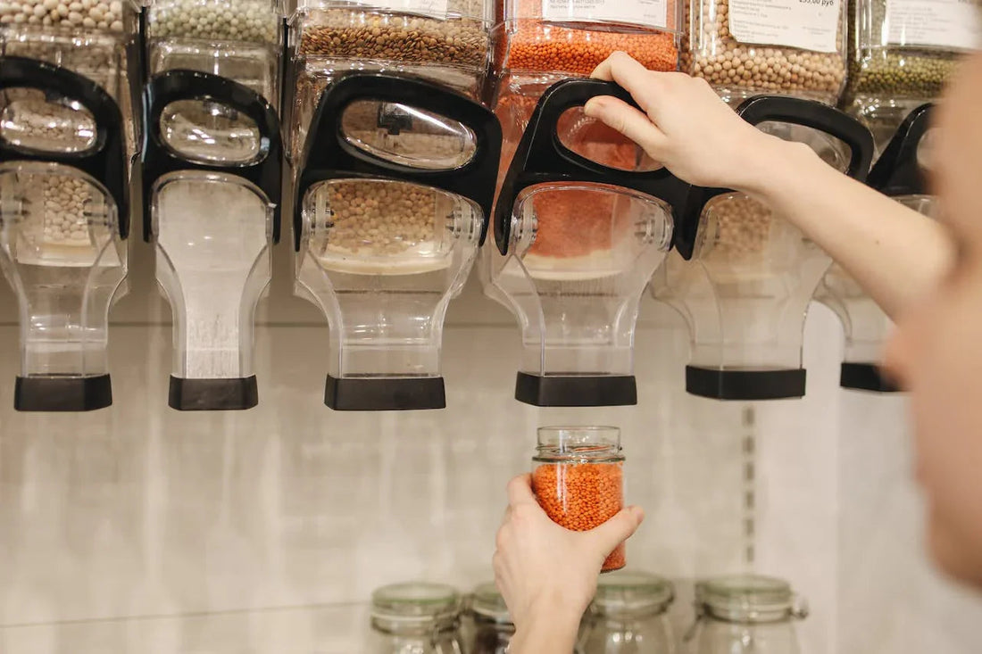 Hand vult glazen pot met rode linzen uit bulkdispenser in zero waste winkel