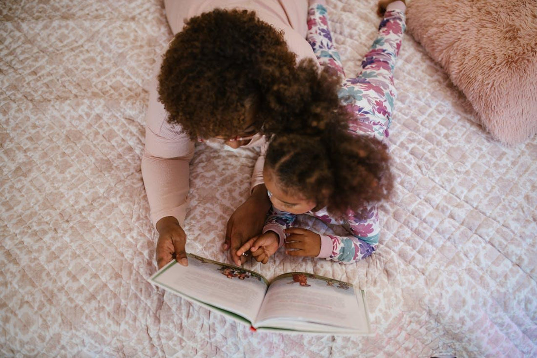 Moeder en dochter lezen samen een boek op bed met bloemenpyjama en zacht dekbedovertrek.