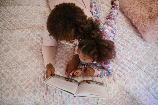 Moeder en dochter lezen samen een boek op bed met bloemenpyjama en zacht dekbedovertrek.
