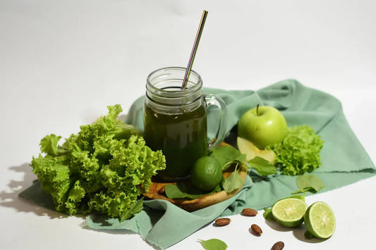 Groene smoothie in een glazen pot met rietje, omgeven door sla, appel, limoen en amandelen