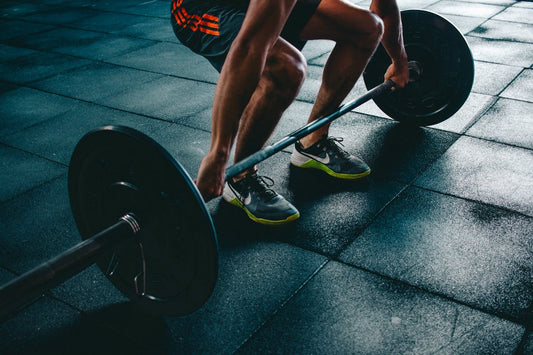 Man in sportschool tilt halterstang op rubberen vloer, krachttraining fitness.